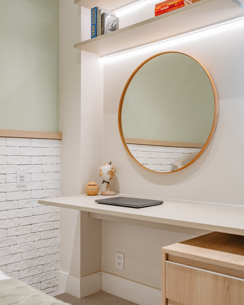 Detalhe de área de trabalho com bancada para notebook, espelho circular decorativo e prateleiras organizadoras com iluminação embutida.
