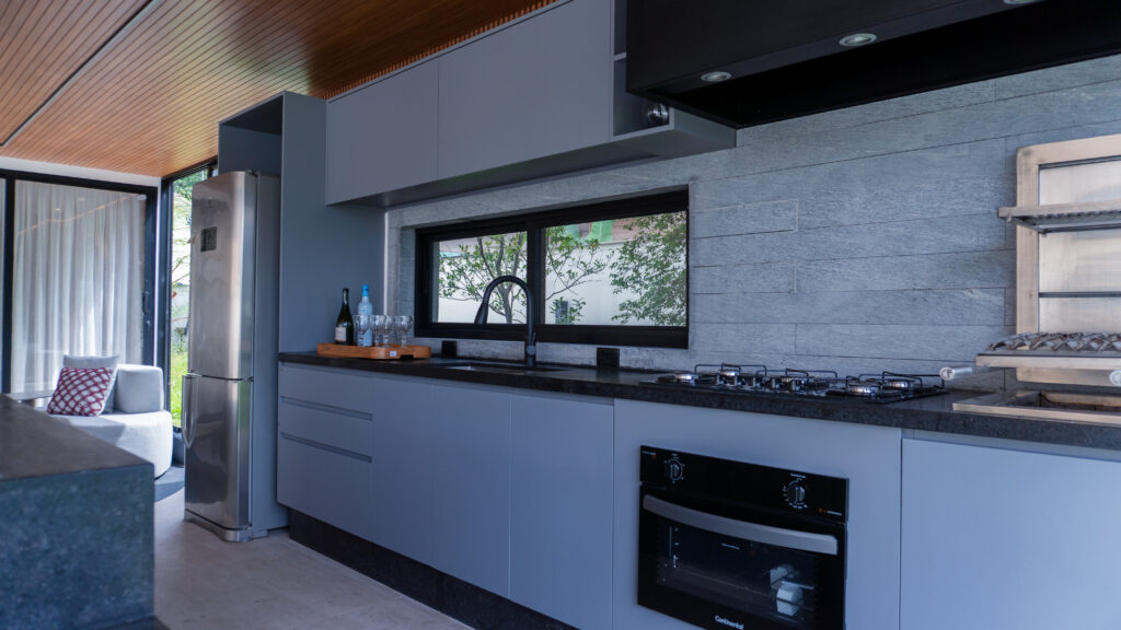 Cozinha planejada Casttini com armários em acabamento Goudí cinza, bancada escura e revestimento de parede em pedra natural cinza, destacando marcenaria moderna e sofisticada.