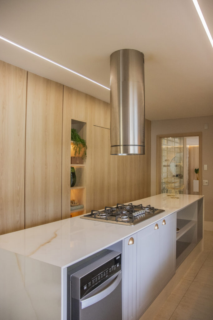 Cozinha moderna com ilha central e marcenaria Casttini em tons claros, destacando a continuidade visual entre painéis e armários para amplitude do ambiente.