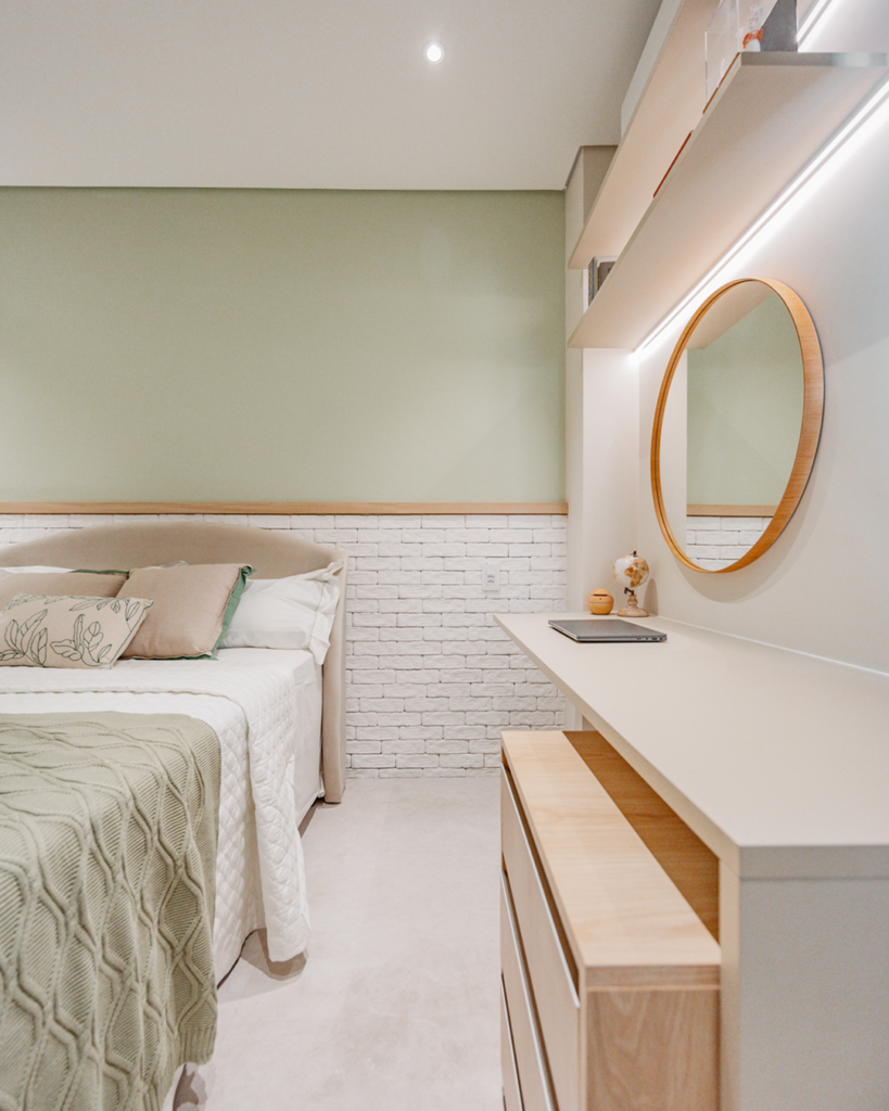 Penteadeira Casttini com bancada ampla em tom off-white, espelho redondo com moldura amadeirada e detalhe de parede em tijolos brancos e verde menta