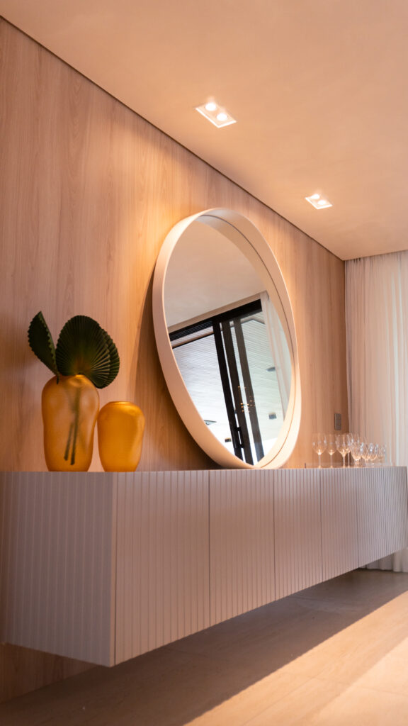 Detalhe lateral de aparador suspenso Casttini com portas ripadas e iluminação embutida em ambiente de alto padrão.