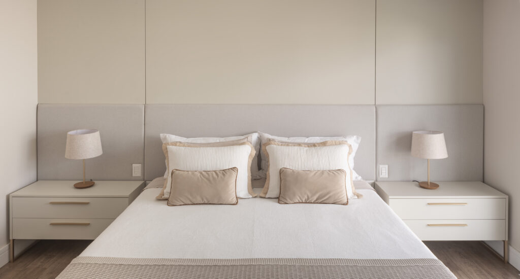 Dormitório planejado Casttini com simetria entre mesas de cabeceira off-white, luminárias e painel estofado, promovendo equilíbrio e pausa no morar contemporâneo.