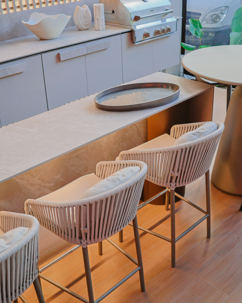 Área gourmet com móveis planejados Casttini em tons de cinza, bancada de pedra clara e banquetas de corda náutica, destacando ergonomia e funcionalidade no layout.