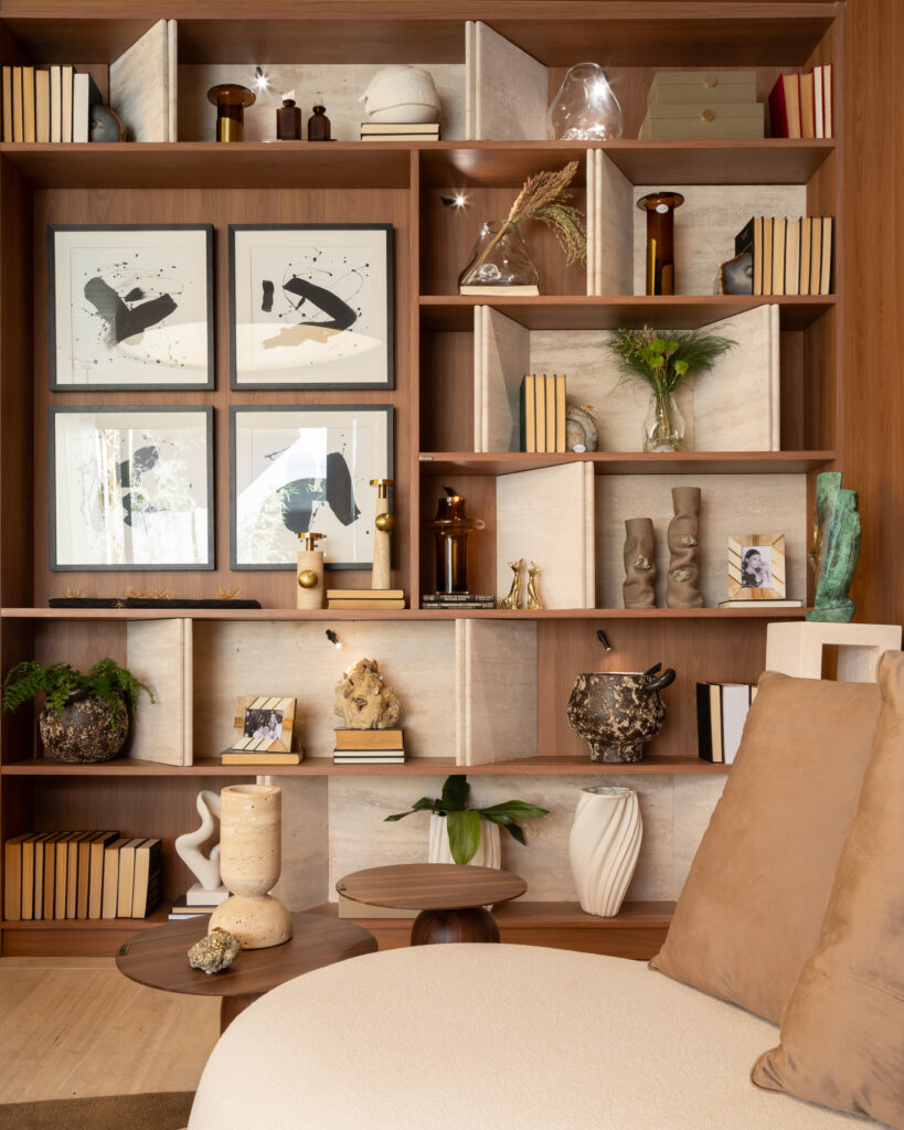 Detalhe de estante em marcenaria sob medida Casttini no acabamento Sequoia com nichos decorados, quadros de arte abstrata e livros, projetada por Vanessa Ortiz para a CASACOR.