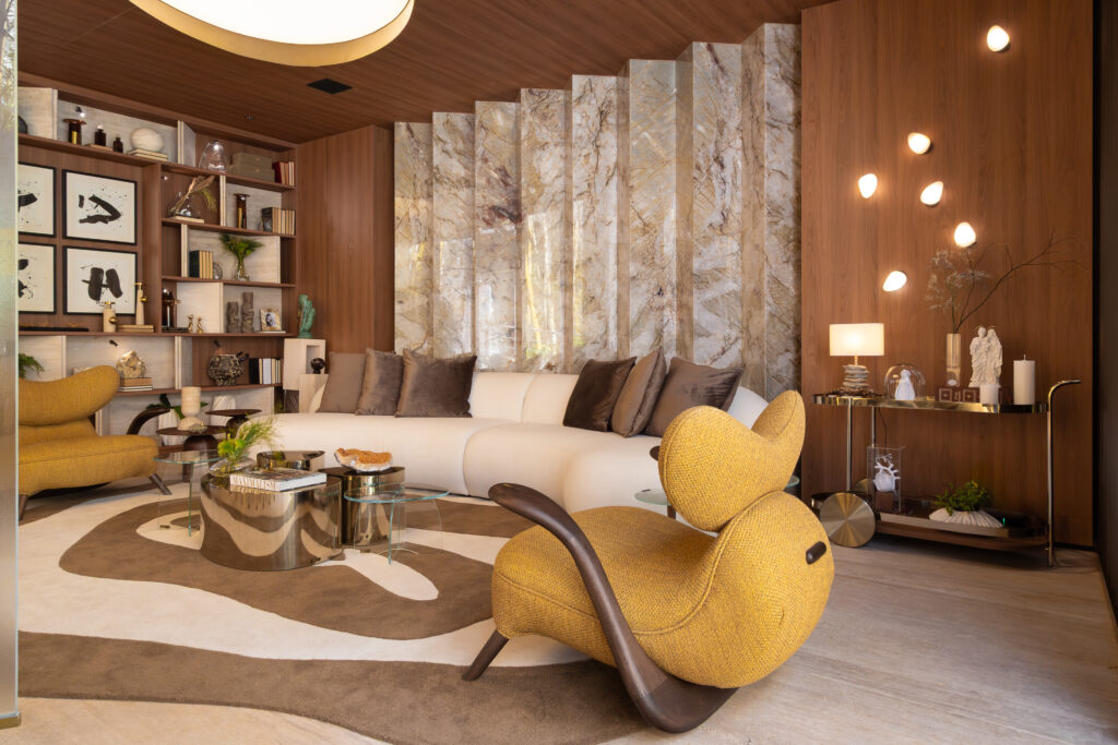 Sala de estar planejada pela arquiteta Vanessa Ortiz com forro de madeira, sofá curvo claro, poltronas texturizadas mostarda e painel de pedra natural retroiluminado com móveis sob medida Casttini.