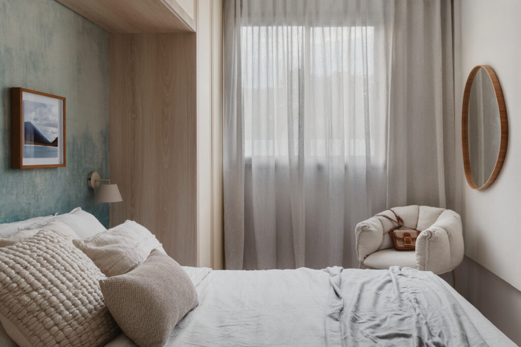 Quarto planejado com cama aconchegante, cabeceira de madeira natural, poltrona de tecido claro e espelho decorativo em projeto da Casttini Moveis Planejados.