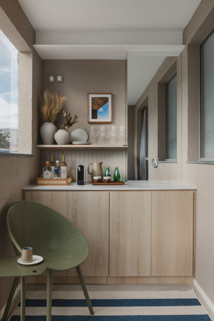 Varanda gourmet integrada com armarios planejados em madeira clara, bancada com bebidas, cadeira verde e decoracao acolhedora por Casttini Moveis Planejados.